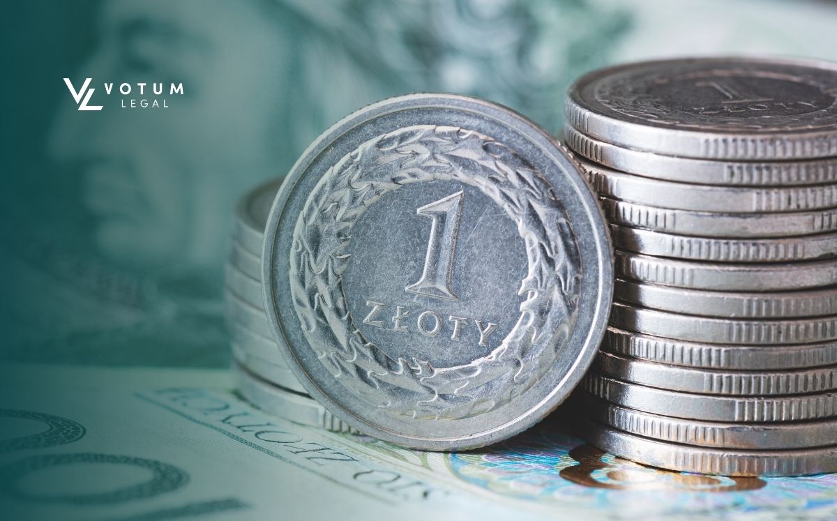 kredyt-konsumencki-odsetki-od-kosztów-kredytu Zbliżenie na monety 1 zł. W tle leżą banknoty o nominale 100 zł
