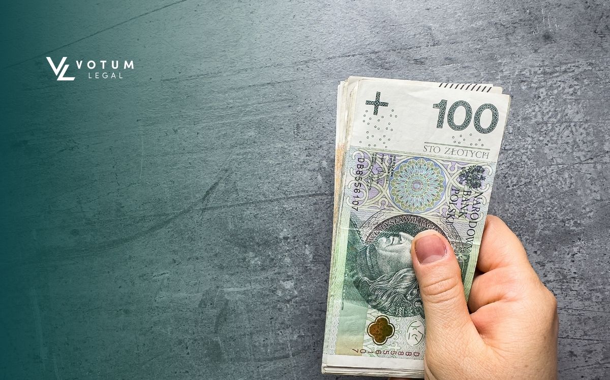 sankcja_kredytu_darmowego_kredyt_konsumencki Dłoń trzymając plik banknotów 100 zł na szarym tle